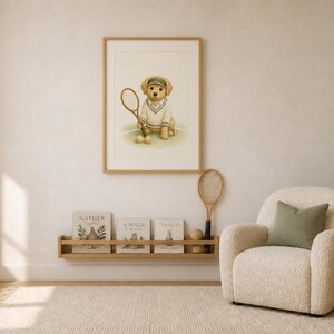 May include: A framed wall print featuring a golden retriever puppy wearing a green visor and a white tennis sweater, holding a tennis racket with two tennis balls at its feet. The print is displayed above a wooden shelf with books and a racket.
