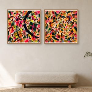 Two square framed abstract art prints hang side by side on a neutral wall above a long cream bench and a small plant table.