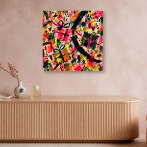 A square abstract art print hangs on a pale wall above a long wooden credenza holding a vase and perfume bottle.