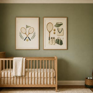 May include: Two framed wall art prints featuring tennis-themed illustrations, including crossed rackets, a ball, a visor, a sweater, shoes, and a duffel bag, displayed above a wooden crib in a room with sage green walls and neutral decor.