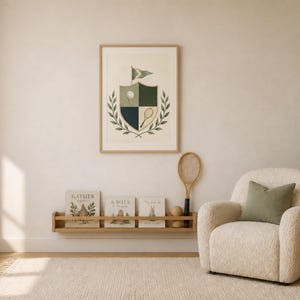 Puede incluir: Una l&aacute;mina de arte mural enmarcada que muestra un escudo con una pelota de golf, una raqueta de tenis y una bandera, rodeado de hojas de laurel. La l&aacute;mina se exhibe sobre un estante de pared de madera con tres libros y una raqueta.