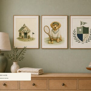May include: Three framed wall art prints featuring a golf clubhouse, a golden retriever puppy wearing a tennis outfit and holding a racket, and a crest with a golf ball and flag. The prints are displayed in light wood frames on a sage green wall.