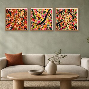 Three matching square abstract art prints with vibrant colors hang in wooden frames on a muted green wall above a beige sofa.