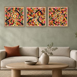 A beige living room featuring a light-colored sofa with an orange pillow and three square colorful abstract prints hanging on the green wall above.