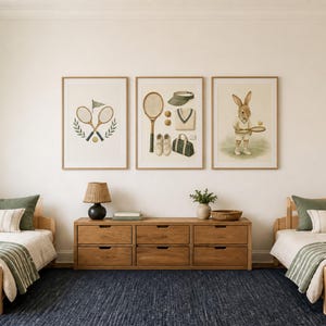 May include: Three framed wall art prints featuring tennis-themed illustrations, including crossed rackets, a collection of tennis gear like a visor and bag, and a rabbit holding a racket, displayed above a wooden dresser between two twin beds.