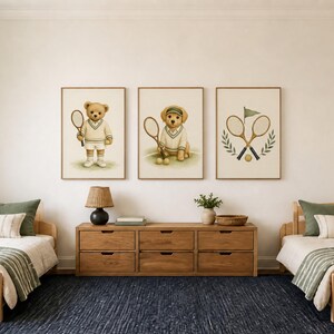 May include: Three framed wall art prints featuring tennis-themed illustrations: a teddy bear holding a racket, a golden retriever puppy with a racket and tennis balls, and two crossed tennis rackets with a flag and laurel leaves on a cream background.