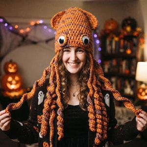 May include: A crochet squid hat in orange and purple yarn featuring two large white and black googly eyes on the front and multiple long, spiraling tentacles hanging down from the sides of the head covering.