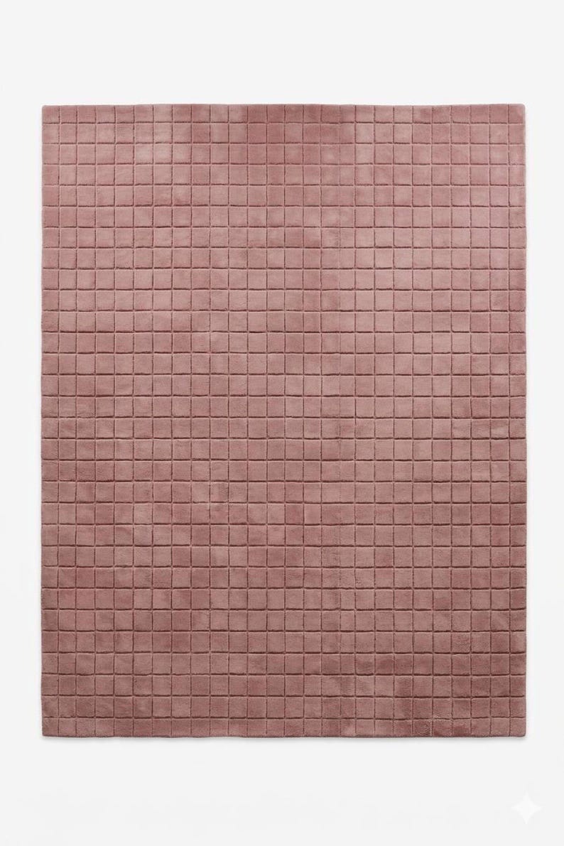 May include: A rectangular area rug in a dusty rose color featuring a uniform grid pattern of small, raised square tufts across the entire surface. The rug has a soft, textured appearance with consistent spacing between each square segment.