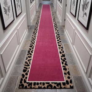 Può includere: Un lungo tappeto da corridoio rettangolare caratterizzato da un pannello centrale in tinta unita magenta vibrante. Il tappeto è incorniciato da un bordo spesso color crema e da un bordo esterno con motivo leopardato nero e beige.