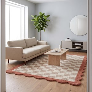 May include: A rectangular area rug featuring a checkered pattern in alternating shades of beige and cream. The rug has a distinct scalloped edge finished in a solid terracotta color, providing a textured border around the entire perimeter.
