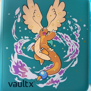 Peut inclure: Un classeur VaultX de couleur sarcelle présentant une illustration centrale d'une créature orange ressemblant à un dragon avec de grandes ailes, entourée d'effets d'énergie violets et blancs tourbillonnants et d'étoiles jaunes.