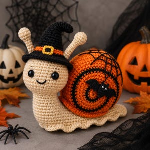 Puede incluir: Un juguete de caracol tejido a ganchillo en color beige que lleva un sombrero de bruja negro con una banda naranja y una hebilla amarilla. La concha es naranja con espirales negras, un diseño de telaraña y un pequeño murciélago negro.