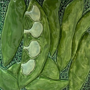 May include: A ceramic tile with a green and white design of a pea pod with three peas inside. The tile has a textured surface and a raised design.