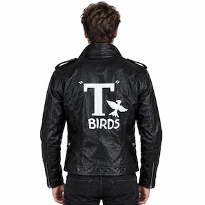 Op de afbeelding: Een zwart leren jack met een grote witte afbeelding op de achterkant. Het ontwerp bevat een prominente letter T, een vogelsilhouet en de tekst BIRDS in het wit gedrukt. Het jack heeft een kraag, schouderkleppen en ritssluitingen.
