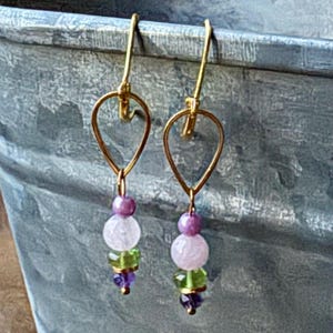 May include: A pair of gold-colored drop earrings. Each earring features a teardrop-shaped frame with a series of colorful beads. The beads include purple, white, green, and amethyst-colored stones, creating a vibrant and elegant accessory.