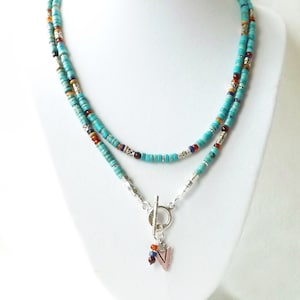 以下が含まれることがあります： ターコイズとシルバーのビーズネックレスに、シルバーの矢じり型のペンダントがついたネックレス。ネックレスは、ターコイズのビーズと小さなシルバーのビーズが2連になっています。