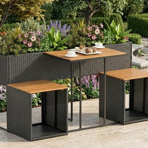 May include: A dark brown woven wicker patio set featuring a central table with a slatted wood top and two matching square stools with wood tops. The table is flanked by two integrated rectangular planters filled with green foliage and pink flowers.