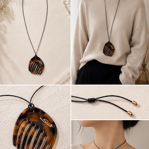 May include: A necklace featuring a tortoise shell patterned comb pendant suspended on a thin black cord. The pendant has a curved shape with multiple teeth and the cursive text "mon Suet" printed in gold. The cord includes adjustable sliding knots.