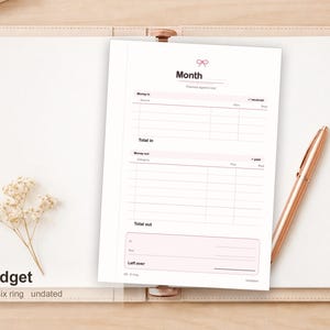 Op de afbeelding: Een wit, ongedateerd A6-budgetplanner-inlegvel met zes ringgaten en een roze strikicoon bovenaan. De pagina bevat secties voor maand, inkomsten, totaal in, uitgaven, totaal uit en overgebleven bedrag met kolommen voor bron, categorie, plan en werkelijk.