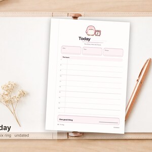 Op de afbeelding: Een witte dagplanner-inlegvel met een afbeelding van een roze cartoonpinguïn en een wekker bovenaan. De pagina bevat de tekst Today, The hours en One good thing, met een verticaal uurschema van 6 tot 18 en drie lege vakjes.