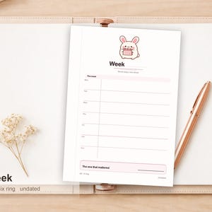 Op de afbeelding: Een witte weekplanner-inzet met een cartoonkonijn dat bovenaan een kalender vasthoudt. De pagina bevat de tekst Week, Seven days, one sheet en The one that mattered, met gelinieerde secties voor de dagen van de week en A6 6 ring Undated.