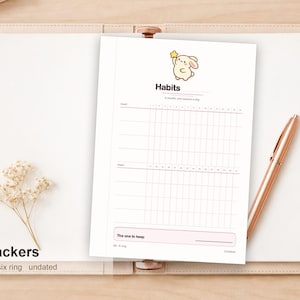 Op de afbeelding: Een ongedateerde A6-habit-tracker-inlegvel met zes ringgaten, voorzien van een cartoonkonijn dat naar een gele ster reikt. De pagina bevat een raster voor het bijhouden van gewoontes over een maand, met de tekst Habits, A month, one square a day en The one to keep.