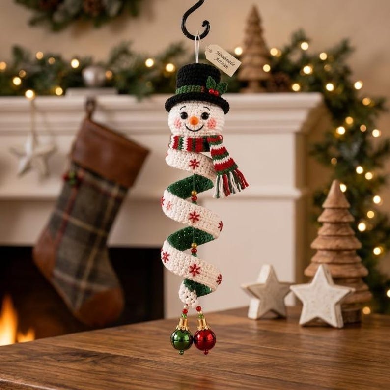 May include: A crocheted snowman ornament with a black top hat, a red and green striped scarf, and a spiral body featuring white and green sections with red snowflake embroidery. The ornament hangs from a hook and includes two small jingle bells.