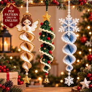 Può includere: Tre ornamenti all'uncinetto da appendere: un angelo con capelli castani e ali bianche, un albero di Natale verde con perline rosse e dorate e una stella gialla, e un fiocco di neve blu e bianco. Testo: PDF PATTERN ONLY IN ENGLISH.