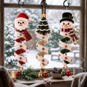 May include: Three hanging crochet ornaments featuring a Santa Claus, a Christmas tree, and a snowman. Each figure has a long, spiraling tail made of cream-colored yarn with red and green snowflake accents, ending in two small, shiny spherical bells.