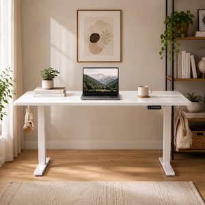 Peut inclure: Un bureau assis-debout blanc réglable en hauteur avec un plateau rectangulaire et deux pieds robustes. Sur le bureau se trouvent un ordinateur portable affichant un paysage de montagne, une petite plante en pot et une tasse en céramique.
