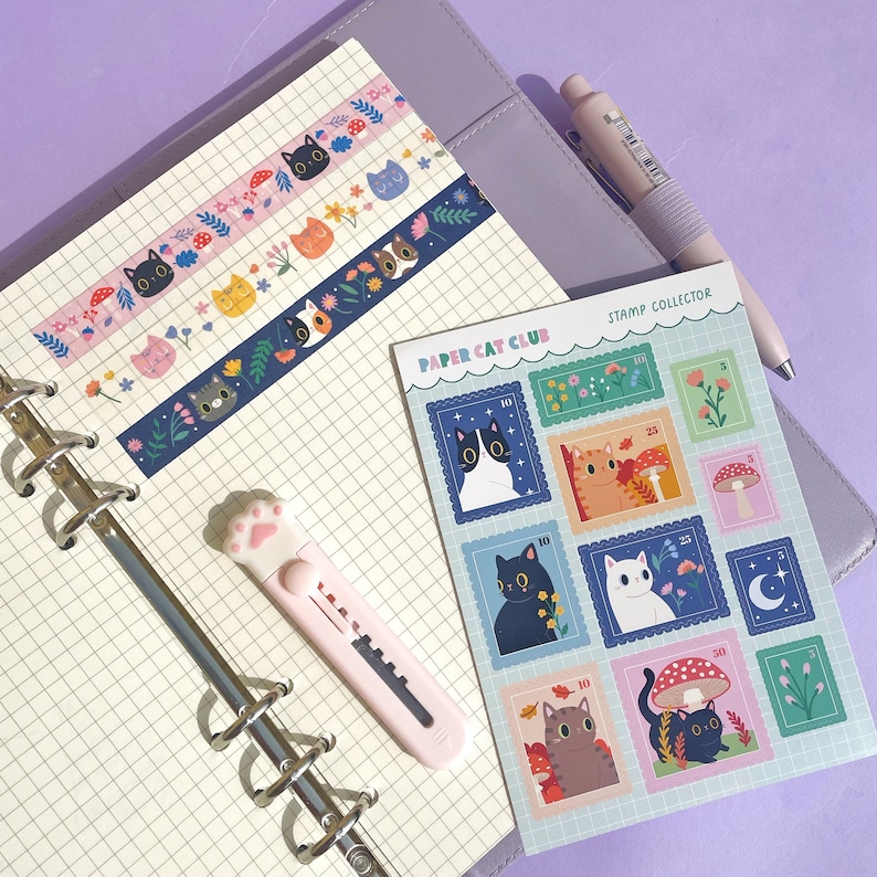 May include: A set of colorful cat-themed washi tape rolls and a sheet of stickers with a blue and white border. The stickers feature illustrations of cats with different expressions and poses. The text on the sticker sheet reads "Paper Cat Club" and "Stamp Collector".