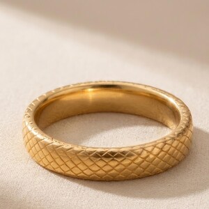 May include: A gold-toned metal ring featuring a continuous, embossed diamond-shaped lattice pattern across its entire outer surface. The band has a smooth, polished interior and a consistent width, showcasing a reflective metallic finish throughout.