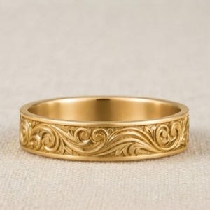 Könnte beinhalten: Ein goldener Bandring mit einem durchgehenden, eingravierten Rankenmuster auf der gesamten Außenfläche. Das Metall hat eine polierte Oberfläche, die die detaillierten, geschwungenen Blatt- und Rankenmotive im Gold hervorhebt.