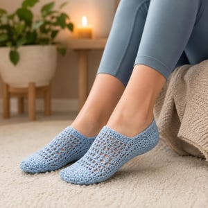 Puede incluir: Un par de zapatillas de ganchillo azul claro con un patrón de celosía calado en la parte superior del pie y una sección sólida de punto en el talón y la puntera. Las zapatillas tienen un diseño de corte bajo bajo el tobillo, hechas de hilo.