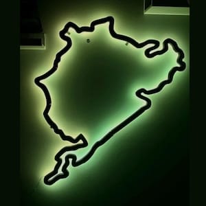 Könnte beinhalten: Ein wandmontiertes Neon-Schild in Form des Streckenverlaufs der Nürburgring Nordschleife. Das Schild besitzt einen durchgehenden schwarzen Rand, der ein sanftes, leuchtendes Licht in einem blassen Grünton abgibt und einen Silhouetteneffekt erzeugt.