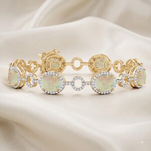 Peut inclure: Un bracelet en or orné d'opales ovales entourées de petits diamants blancs. Le design alterne entre ces sertissages d'opales et des maillons circulaires en or, terminé par un fermoir à cliquet sécurisé sur le côté gauche de la pièce.