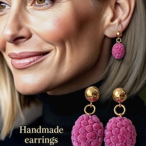 Op de afbeelding: Een paar handgemaakte oorbellen met een gepolijste goudkleurige metalen knop verbonden aan een getextureerde, framboosroze ovale hanger met een hobbelig, bessenachtig oppervlak. De tekst "Handmade earrings" is zichtbaar in de linkerbenedenhoek.