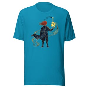 Puede incluir: Una camiseta de manga corta color azul cerceta con un gráfico de una persona de cabello rojo ondeante que viste un abrigo oscuro con constelaciones blancas. La figura sostiene una guitarra acústica dorada brillante con notas musicales.