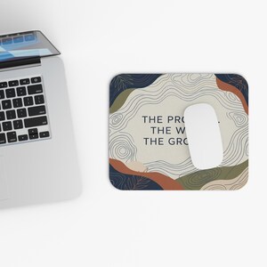 Op de afbeelding: Een rechthoekige muismat met een topografisch kaartpatroon in marineblauw, olijfgroen en terracotta. In het midden staat de tekst THE PRO... THE W... THE GRO... met een witte computermuis die op het oppervlak rust.