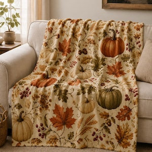 May include: A cream-colored throw blanket featuring a repeating autumn-themed pattern of orange and green pumpkins, vibrant red and brown maple leaves, wheat stalks, and small clusters of red berries spread across the entire fabric surface.