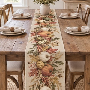May include: A rectangular table runner featuring a printed design of autumn harvest elements including orange, green, and white pumpkins, gourds, wheat stalks, red berries, and colorful fall leaves on a light beige fabric background.