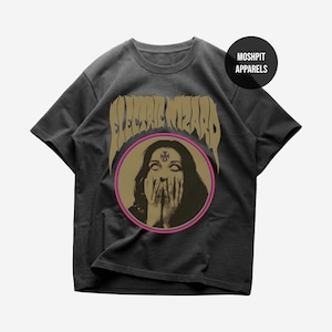 Könnte beinhalten: Ein anthrazitfarbenes Kurzarm-T-Shirt mit dem Schriftzug ELECTRIC WIZARD in goldener Schrift über einer kreisförmigen Grafik einer Person, die sich die Hände vor den Mund hält. Ein violettes Symbol ist auf der Stirn. Ein schwarzer Kreis enthält MOSHPIT APPARELS.