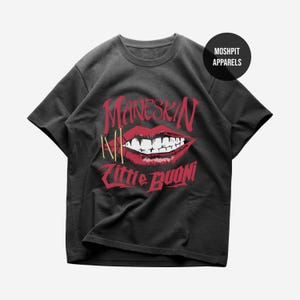 Könnte beinhalten: Ein anthrazitfarbenes Kurzarm-T-Shirt mit einer Grafik aus roten Lippen und weißen Zähnen. Der Text lautet Måneskin und Zitti e Buoni in einer stilisierten roten Schrift. Ein kleines schwarzes kreisförmiges Logo oben rechts zeigt MOSHPIT APPARELS.