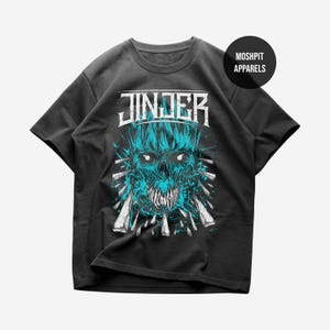 Op de afbeelding: Een zwart t-shirt met korte mouwen en een grafische print van een blauw-witte schedel met scherpe tanden en stekels. De tekst JINJER staat in het wit boven de schedel gedrukt en een cirkelvormig logo met de tekst MOSHPIT APPARELS staat rechtsboven.
