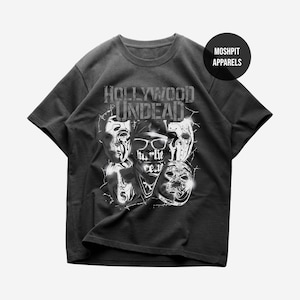 May include: A black short-sleeved t-shirt featuring a graphic print of five masks and the text "HOLLYWOOD UNDEAD" and "hurlie ceu". A circular black logo in the top right corner contains the white text "MOSH PIT APPARELS" in a sans-serif font.