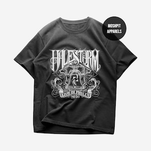 May include: A black short-sleeve t-shirt featuring a white graphic print of the band name Halestorm above an illustration of the Liberty Bell with the text Live in Philly 2010. A circular black logo in the top right corner reads Moshpit Apparels.