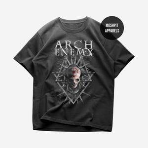 May include: A black short-sleeve t-shirt featuring the text ARCH ENEMY in white above a graphic of a skull with a red target symbol on the forehead, set against a geometric starburst design. A black circular logo reads MOSHPIT APPARELS.