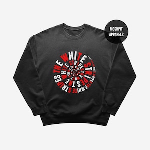 May include: A black crewneck sweatshirt featuring a circular graphic design on the chest. The text "THE WHITE STRIPES" is repeated in a spiral pattern in alternating red and white colours. A circular black logo reads "MOSH PIT APPARELS".