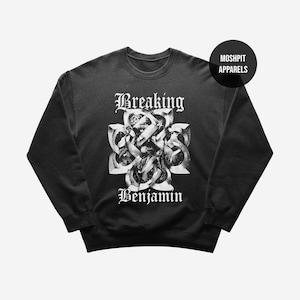 Può includere: Una felpa nera a girocollo con una stampa grafica bianca sul petto. Il design include il testo Breaking Benjamin in un carattere gotico sopra e sotto un'illustrazione centrale a forma di nodo. Un logo circolare riporta MOSHPIT APPARELS.