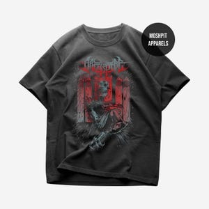 May include: A charcoal gray short-sleeve t-shirt featuring a graphic print of a skeletal figure in red and white tones. The design includes stylized text at the top and a circular logo in the upper right corner with the text MOSHPIT APPARELS.